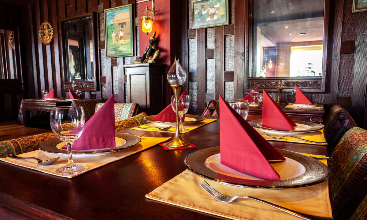 Gedeckter Tisch mit roten Servietten, goldenen Platzsets und Messingkaraffe vor holzvertäfelter Wand
